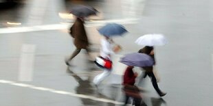 Fußgänger mit Regenschirmen überqueren einen Platz.