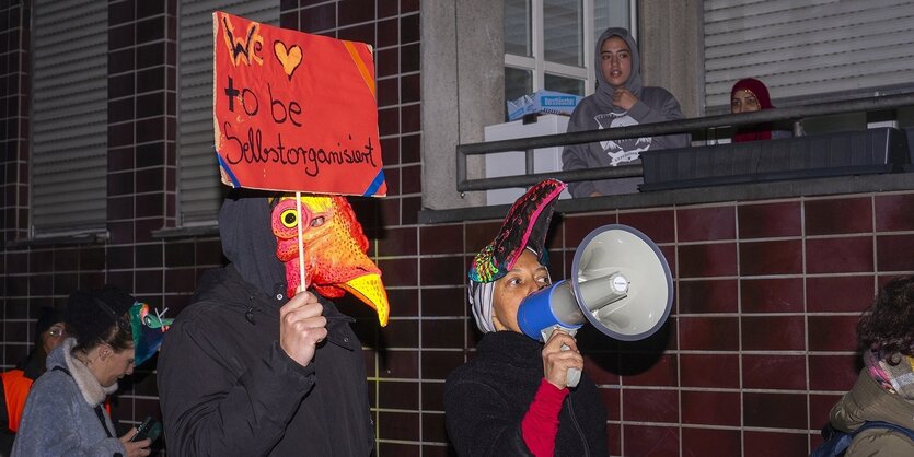 Auf einer Demonstration laufen maskierte Menschen mit Schildern in der Hand