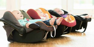 Drei gut gelaunte Babies liegen in Babyschalen, die nebeneinander stehen