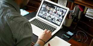 Ein Mann sitzt an seinem Schreibtisch vor senem Labtop, auf dem die Teilnehmer eines Zoom Meetings zu sehen sind