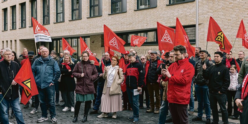 Menschen stehen vor einem Gebäude und halten die roten Fahnen der IG Metall.