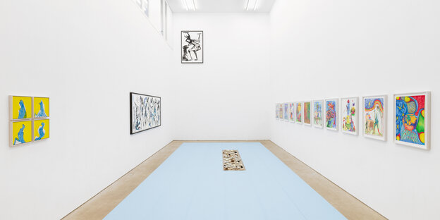 Blick in einen Ausstellungsraum. Auf dem Boden liegen hellblaue Yogamatten zu einem Rechteck geformt aus. In ihrer Mitte liegen runde Skulpturen aus Ton und Luftballons. An der rechten Wand sind bunte Zeichnungen zu sehen. An der linken Wand vier gelbe Ma