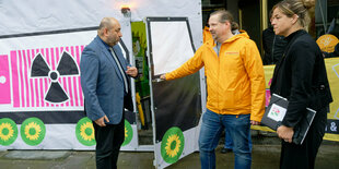 Drei Menschen vor Plakatwand mit Grünen-Logo und Radioaktivitäts-Zeichen