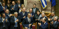 Der griechische Ministerpräsident Kyriakos Mitsotakis (M) wird von den Abgeordneten seiner Partei während einer Parlamentssitzung beklatscht