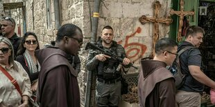 Ein Mitglied der israelischen Sicherheitskräfte steht bewaffnet an der Wand, während christliche Gläubige an der Karfreitagsprozession in der Altstadt von Jerusalem teilnehmen