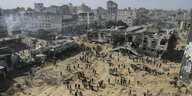 Menschen aus der Luft aufgenommen,stehen auf sandigem Boden, im Hintergrund Trümmer von Hochhäusern