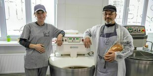 Ein Mann und eine Frau stehen lächelnd vor einer Maschine zum Brotbacken, der Mann hat ein Brot in der Hand