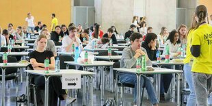 Studierende sitzen in einm Saal an Einzeltischen und warten auf die Arbeitsbögen für den Medizinertest