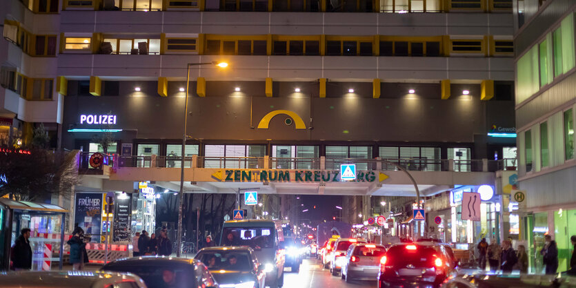 Eine Straße bei Nacht, sie führt unter einem großen Haus hindurch, dort steht im ersten Stock in Leuchtbuchstaben "Polizei"