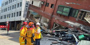 Drei gelbgekleidete Feuerwehrmänner vor einem eingestürzten Haus in Hualien; Taiwan