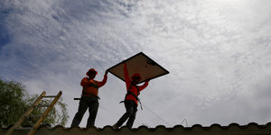 Zwei Männer tragen ein Solar-Panel auf ein Dach.