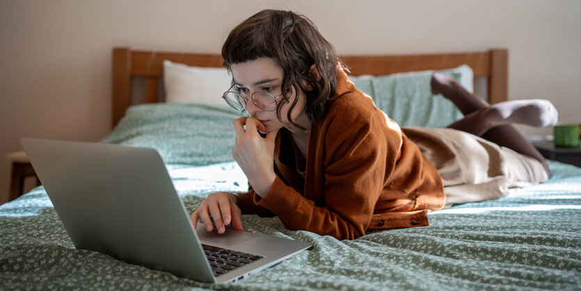 Ein Teenager liegt auf einem Bett und schaut interessiert in einen Labtop.