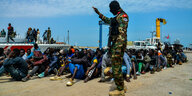 Flüchtlinge sitzen an einem tunesischen Hafenkai, bewacht von Polizei