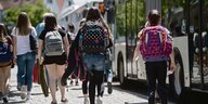 Schülerinnen mit Ranzen auf dem Rückken laufen auf einen Bus zu