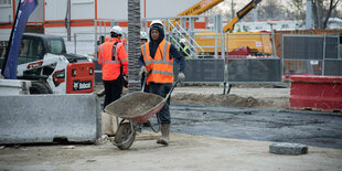 Auf einer Baustelle schiebt ein Bauarbeiter eine Schubkarre.