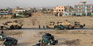 Sandfarbene Jeeps und gepanzerte Fahrzeuge vor ein paar Gebäuden in der Wüste