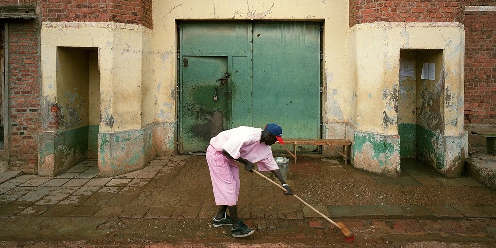 Ein mann in rosafrbener Häftlingskleidung fegt vor dem Eingang des gefängnisses in Kinshasa