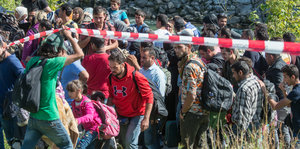 Flüchtlinge laufen unter einem rot-weißen Flatterband durch