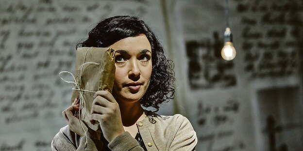 Eine Schauspielerin auf einer Bühne drückt ein verpacktes Buch an ihr Gesicht.