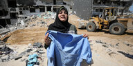 Eine Frau steht mit einem Kleidungsstücken in den Trümmern von Gaza