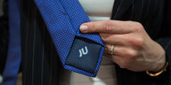 Eine Hand dreht eine Krawatte, auf deren Rückseite die Abkürzung "BU" gestickt ist