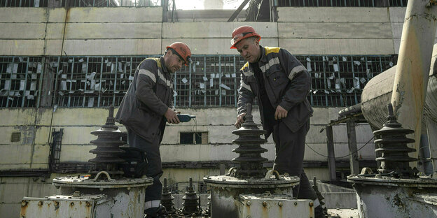 Zwei Arbeiter mit Helm überprüfen einen Transformator, der durch einen russischen Raketenangriff auf das DTEK-Kraftwerk in der Ukraine beschädigt wurde