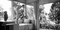 SChwarz-Weiß-BIld: Eine Frau steht auf einem Sofa und setzt an zu springen. Sie befindet sich in einem modernistischen Wohnhaus in Los Angeles, ca. 1942
