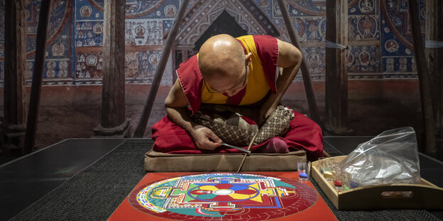 Ein Mönch arbeitet an einem Mandala aus buntem Sand