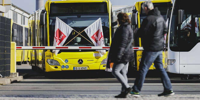 Menschen laufen an einem BVG-Bus mit Verdi-Bannern vorbei