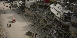 Menschen ziehen durch eine zerstörte Stadt. Fotografiert von schräg oben, so dass die Menschen klein neben den Ruinen sind.