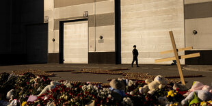 Ein Holzkreuz und Blumen liegen vor einem Gebäude auf dem Boden