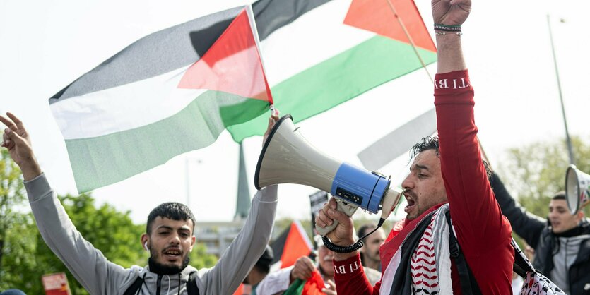 Zwei Demonstranten mit Megaphon vor palästinensischen Fahnen