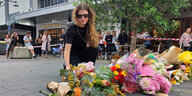 Eine junge Frau mit verweintem GEsicht und Sonnebrille legt Blumen auf der Strasse ab