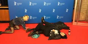 Die drei Bandmitglieder des Trios Cuntraoches kugeln am Boden über einen roten Teppich auf der Berlinale. Hinter ihnen steht eine blaueb Stellwand mit Berlinale-Logos.