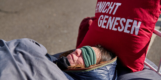 Eine Frau liegt bei einem Protest nuit Schlafbrille in einem Bett.