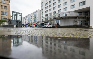 Über Straßenpflaster und ein Pfütze hinweg geht der Blick zu einem mehrstöckigen schmucklosen Gebäude