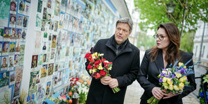 Ein Mann und eine Frau haben Blumen in der Hand und laufen in Kyjiw an einer Mauer entlang