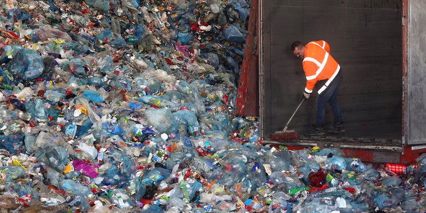 Ein Mann kehrt in einem Berg leerer Plastikflaschen.