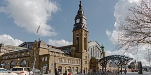 Ein altes, graues Gebäude mit Uhrenturm und Menschen davor.