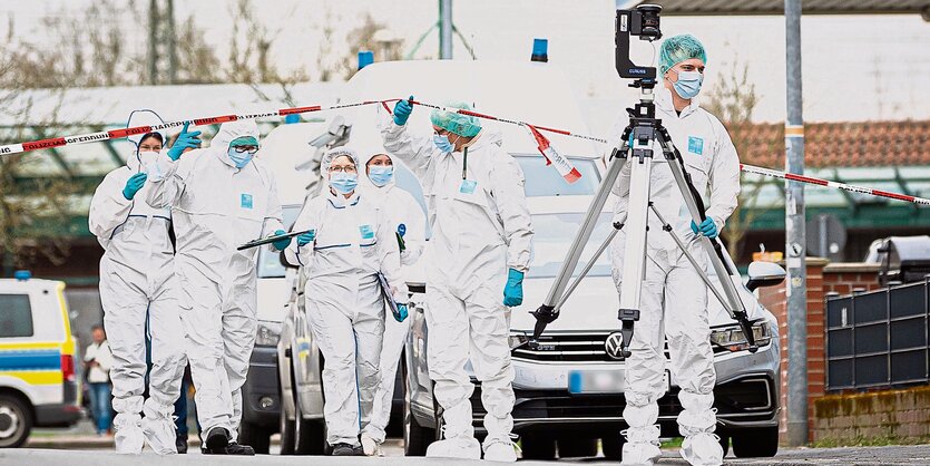 Beamte der Spurensicherung in Schutzkleidung gehen unter einem Absperrband durch