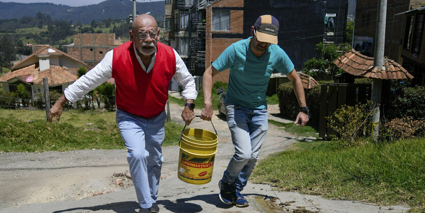 Zwei Männer tragen einen gelben Eimer mit Wasser.