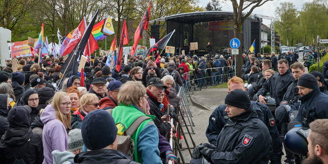 Menschen mit vielen Plakaten und Fahnen stehen vor Polizisten und Polizistinnen an einer Absperrung