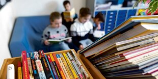 Drei Kinder sitzen auf einem blauen Sofa mit Büchern in der Hand