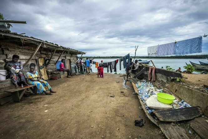 Frauen sitzen auf Bänken , im Hintergrund ein See, ein Boot gefüllt mit Plastikmüll steht auf der ERde