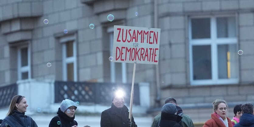 Ein Teilnehmer einer Kundgebung hält ein Plakat mit der Aufschrift „Zusammen für Demokratie“ hoch.