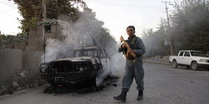 Ein Mann mit einer Waffe neben einem abgebrannten Auto