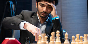 Gukesh zieht mit dem rechten Arm eine Schachfigur, mit dem linken stützt er seinen Kopf