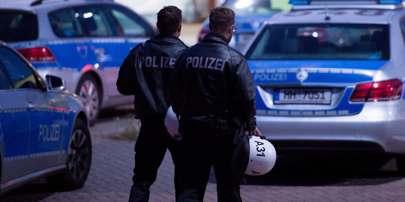 Polizisten stehen vor Polizeiautos