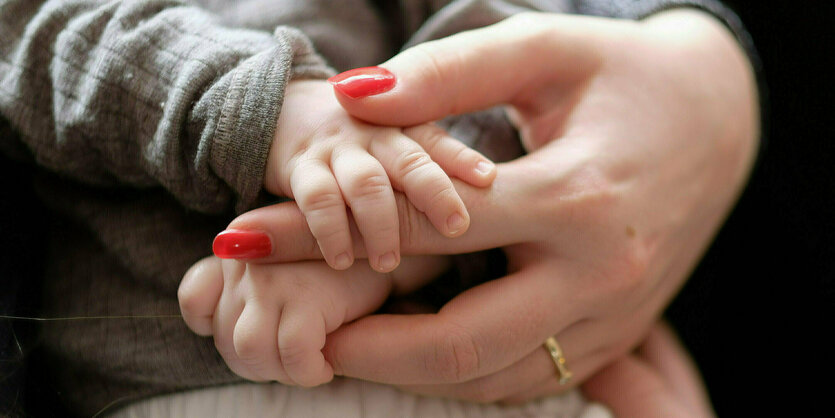 Die kleinen Hände eines Babys greifen nach einer Hand mit lackierten Fingernägeln