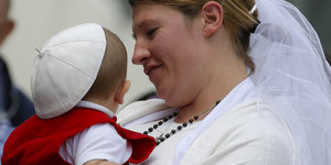 Eine Frischvermählte mit Baby auf dem Petersplatz. Papst Franziskus hat dem Kind sein Käppchen aufgesetzt.